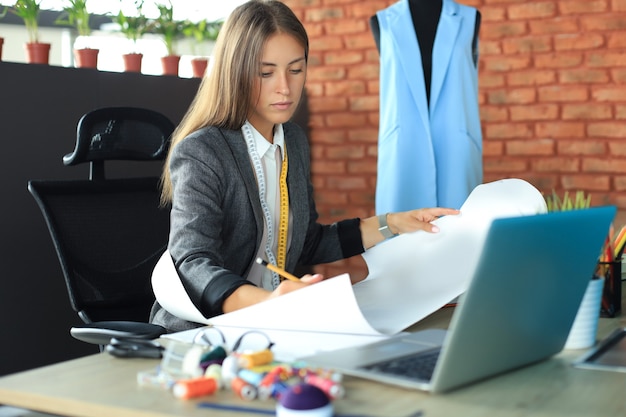 Schöne junge Designerin, die an Skizzen arbeitet, während sie in ihrem Studio sitzt.