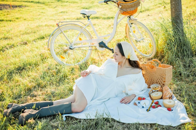 Schöne junge dunkelhaarige Frau beim Picknick auf dem Feld Model in stilvollen Kleidern mit Fahrrad Sommer