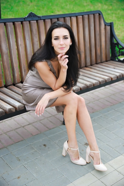 Schöne, junge dunkelhaarige Frau in einem Sommerkleid, das auf einer Bank sitzt