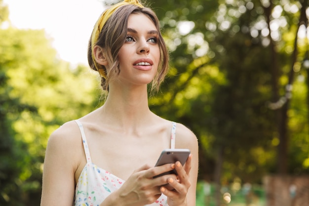 schöne junge erstaunliche Frau im grünen Park, die mit dem Handy plaudert.