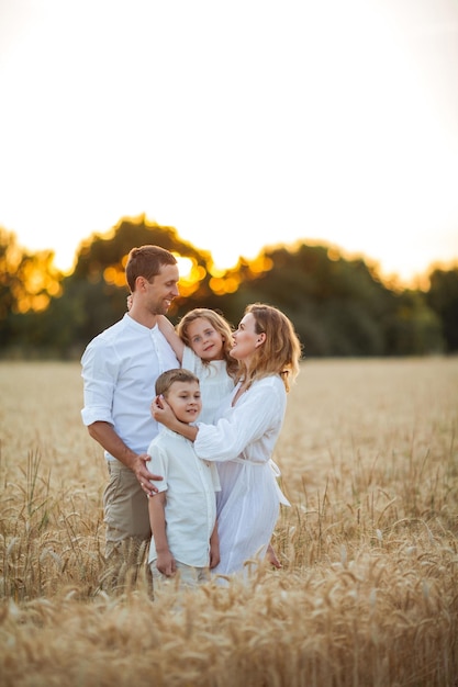 Schöne junge Familie bei Sonnenuntergang in einem Weizenfeld Glückliche Eltern mit zwei Kindern, einem Jungen und einem Mädchen in leichter Kleidung Sommer