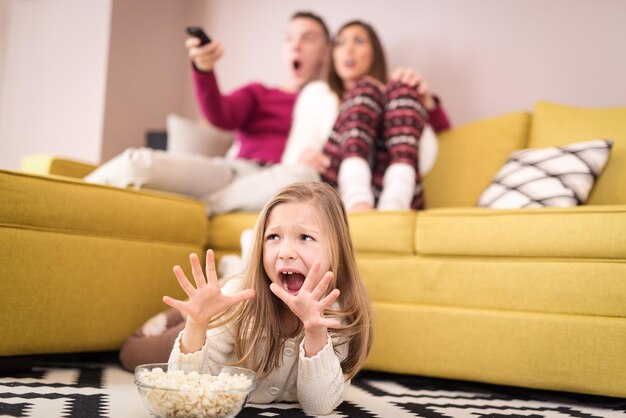 Schöne junge Familie, die sich im Wohnzimmer einen Gruselfilm ansieht. Selektiver Fokus.