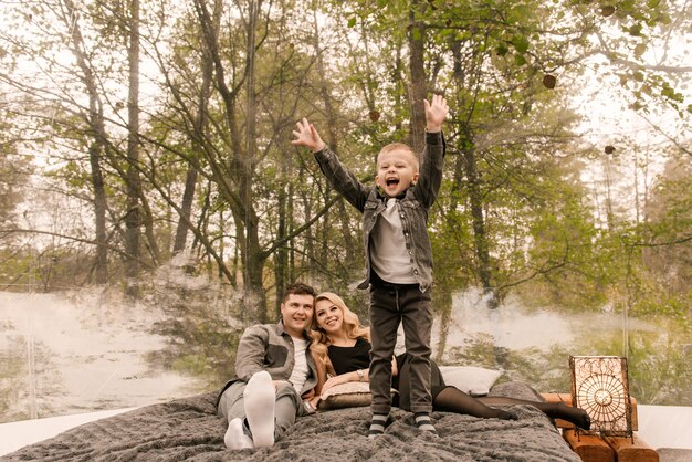 Schöne junge Familie Mann Frau und Sohn entspannen im Wald in der Natur in einem großen runden Zelt mit einem Bett und einem Herd zum Kochen, Picknick, Camping