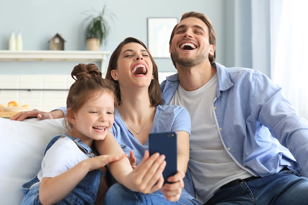 Schöne junge Familie mit kleinem Kind, das zu Hause auf der Couch ein Selfie mit einem Smartphone macht.