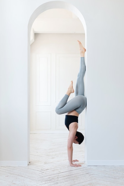 Schöne junge Fitness-Bloggerin, die im hellen Raum einen schwierigen Handstand macht. Konzept des regelmäßigen Trainings und der Willenskraft.