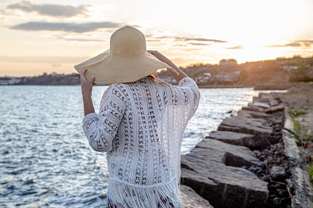 Schöne junge Frau am Meer bei Sonnenuntergang. In einen langen Rock und Hut gekleidet.