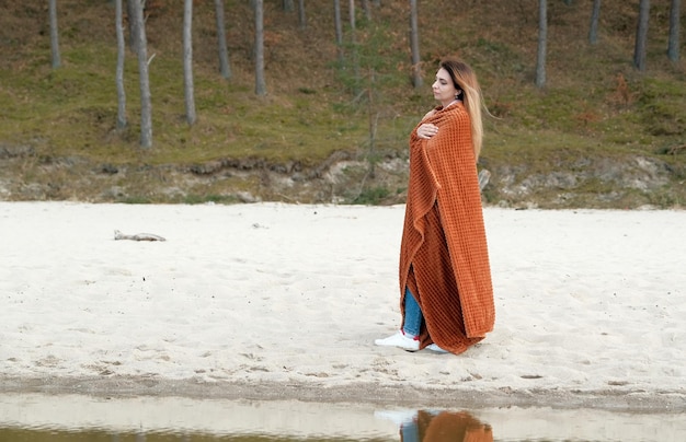 Schöne junge Frau bedeckt mit Decke am Strand