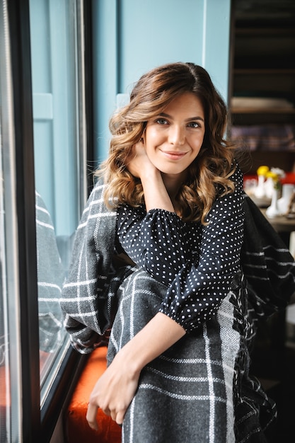 Schöne junge Frau bedeckt mit Decke, die im Café drinnen sitzt