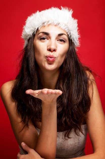 Schöne junge Frau beim Weihnachtsmann-Hutlächeln. Weihnachtsgeschichte. Postkarte. Vertikale. Rot .