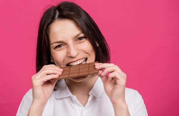 Schöne junge Frau beißt eine Tafel Schokolade