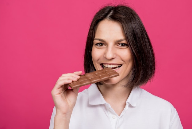 Schöne junge Frau beißt eine Tafel Schokolade