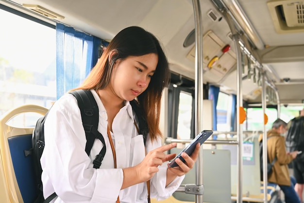 Schöne junge Frau benutzt ein Smartphone, während sie einen Bus in der Stadt fährt