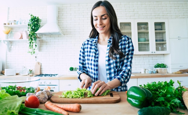 Schöne junge Frau bereitet Gemüsesalat in der Küche zu. Gesundes Essen. Veganer Salat. Diät. Diät-Konzept. Gesunder Lebensstil. Kochen zu Hause. Essen zubereiten. Schneiden von Zutaten auf dem Tisch