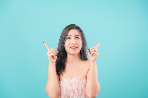 Schöne junge Frau des asiatischen glücklichen Porträts, die ihren Zeigefinger oben lokalisiert auf blauem Hintergrund mit Kopienraum für Text steht