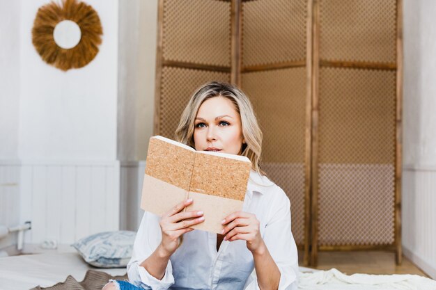 Schöne junge Frau, die auf dem Sofa in der leichten Kleidung sitzt und in ein Notizbuch schreibt