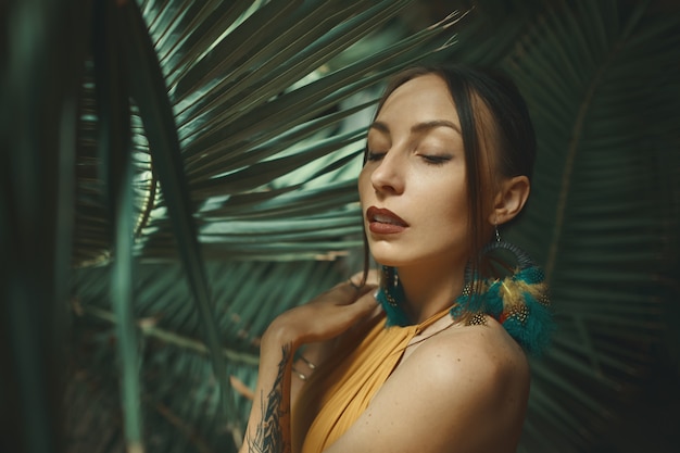Schöne junge Frau, die auf einem Hintergrund des exotischen Palmblattes aufwirft