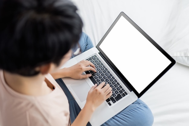 Schöne junge Frau, die auf ihrem Bett sich entspannt und mit ihrem Laptop arbeitet.