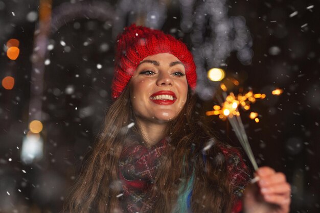 Schöne junge Frau, die bei Schneefall mit Wunderkerzen auf der Straße spielt