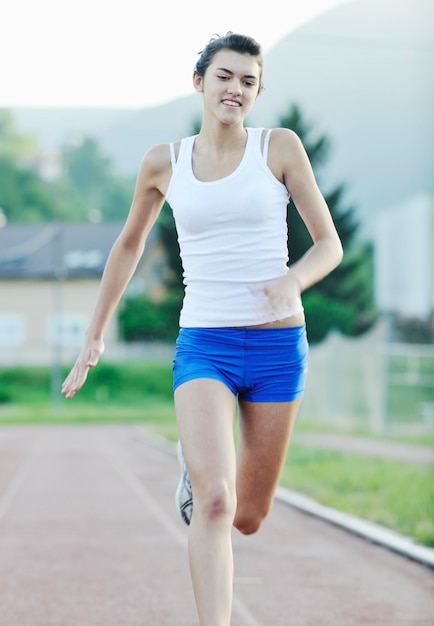 Schöne junge Frau, die bei Sonnenaufgang auf der Leichtathletikbahn im Stadion joggt und läuft