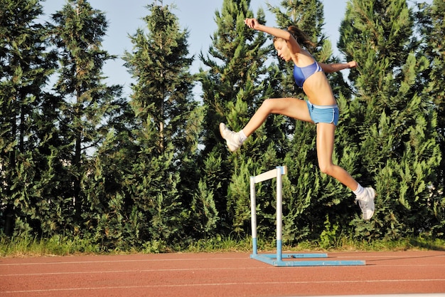 Schöne junge Frau, die bei Sonnenaufgang auf der Leichtathletikbahn im Stadion joggt und läuft