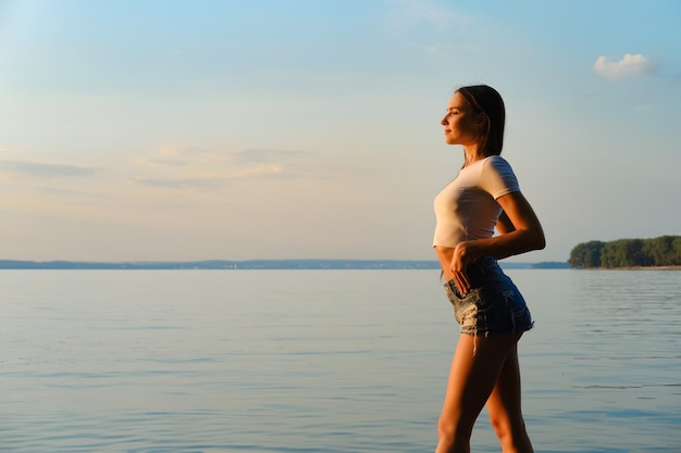 Schöne junge Frau, die bei Sonnenuntergang die frische Abendluft am See genießt