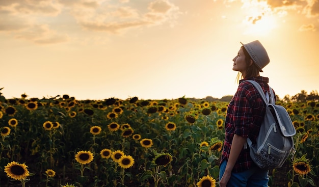 Schöne junge Frau, die die Natur auf dem Sonnenblumenfeld bei Sonnenuntergang genießt