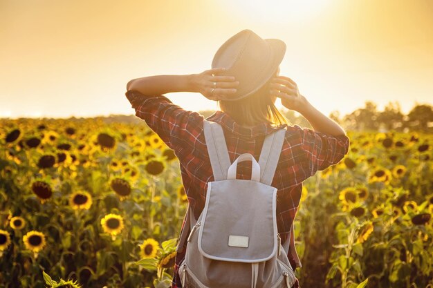 Schöne junge Frau, die die Natur auf dem Sonnenblumenfeld bei Sonnenuntergang genießt