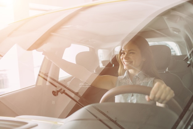 Schöne junge Frau, die ein Auto am Autohaus kauft. Weibliches Modell sitzt sitzt im Innenraum des Autos