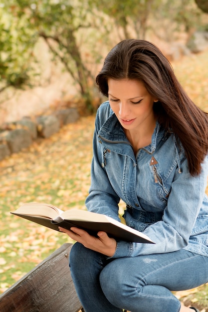 Schöne junge Frau, die ein Buch im Park am Fall liest