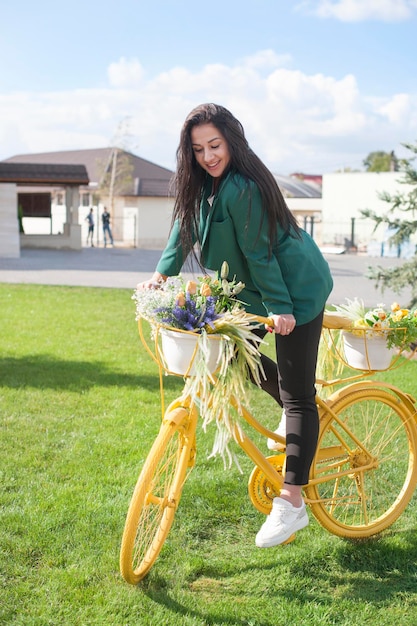 Schöne junge Frau, die ein gelbes Fahrrad mit Blumenkorb fährt