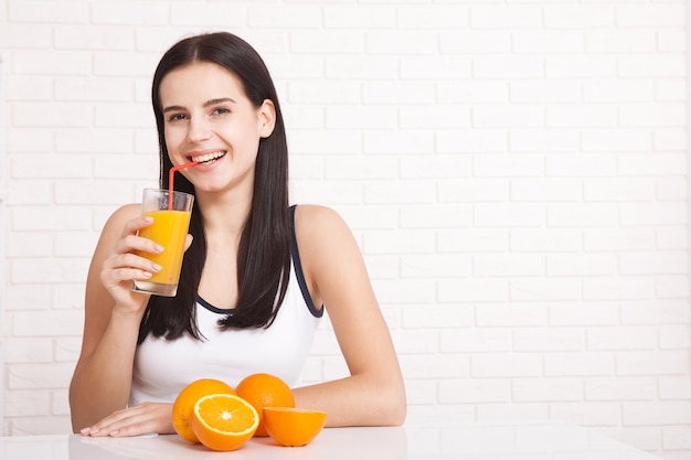 Schöne junge frau, die ein glas mit orangensaft in ihrer hand hält und lächelt