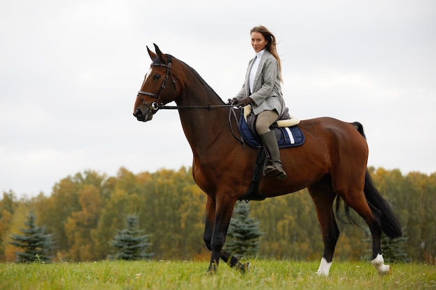 Schöne junge Frau, die ein Pferd auf dem Feld reitet Seitlich zur Kamera Freiheitsfreudenbewegung