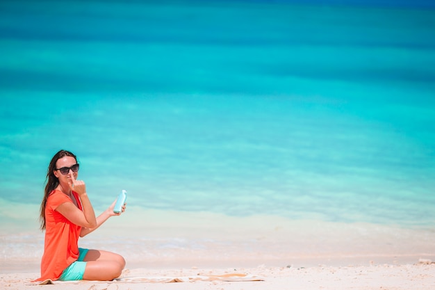 Schöne junge Frau, die eine Sonnencreme hält, die am tropischen Strand liegt