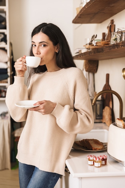 Schöne junge Frau, die eine Tasse Kaffee in der Küche trinkt