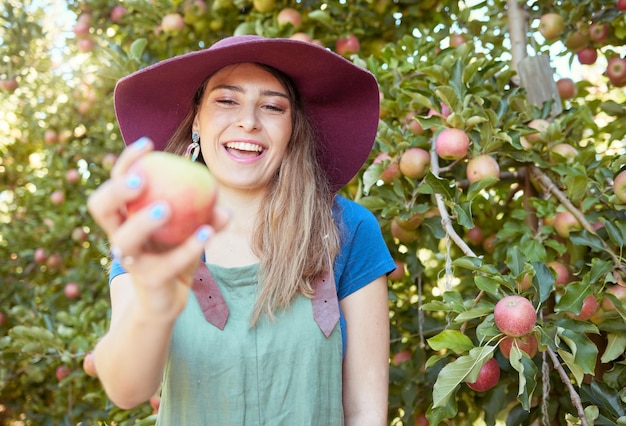 Schöne junge frau, die einen apfel auf einem bauernhof hält glückliche dame, die äpfel in einem obstgarten pflücken frisches obst produzieren, das in einem feld auf ackerland wächst die agrarindustrie produziert in der erntezeit