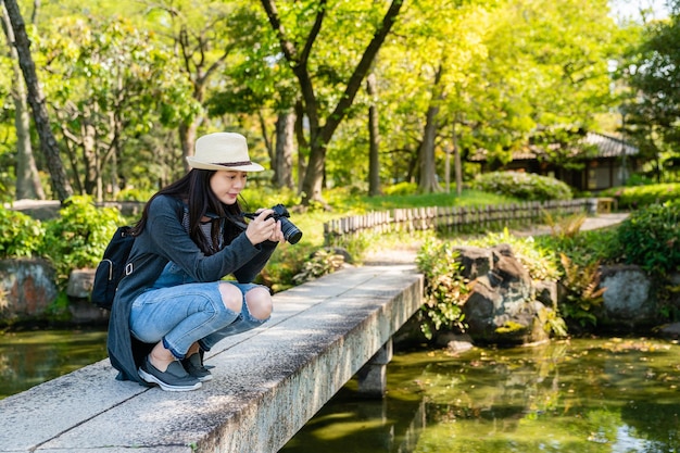 schöne junge frau, die fotos in einem erstaunlichen japanischen garten mit vielen pflanzen und schönem gebäude macht.