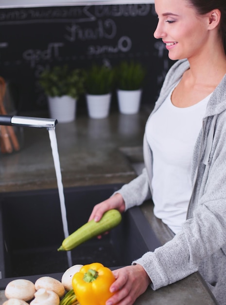 Schöne junge Frau, die Gemüse für Salat wäscht, während sie in der Küche steht