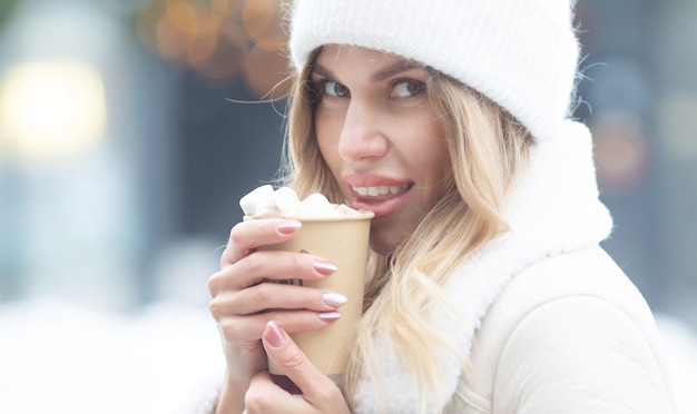 Foto schöne junge frau, die heißen kakao draußen trinkt. weihnachten.