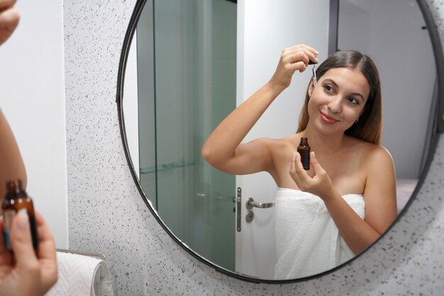 Foto schöne junge frau, die hyaluronsäure mit einer pipette im badezimmer anwendet