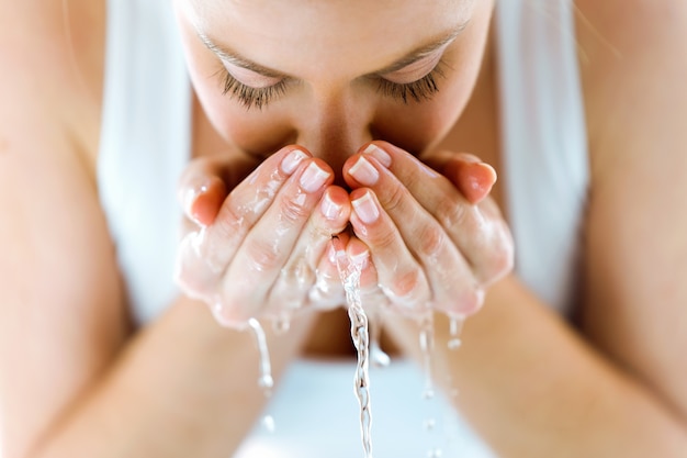 Schöne junge frau, die ihr gesicht spritzt wasser in einem hauptbadezimmer wäscht.