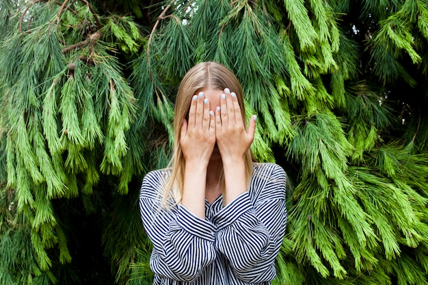 Foto schöne junge frau, die ihr gesicht steht im wald gegen tannenbäume versteckt.