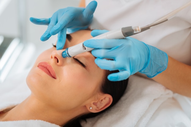 Schöne junge Frau, die ihre Augen schließt, während sie eine hydrafacial Prozedur hat