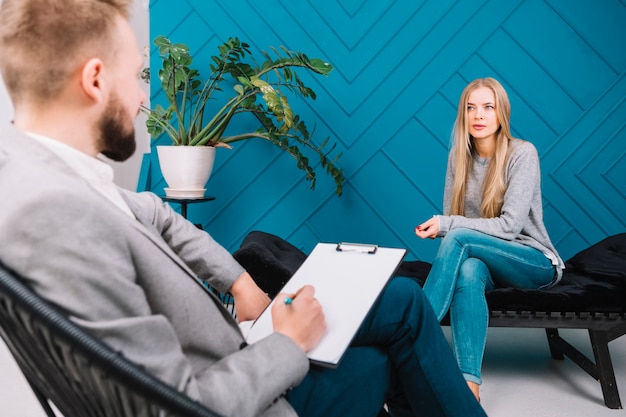 Foto schöne junge frau, die ihre probleme mit dem männlichen psychologen bespricht, der auf stuhl sitzt