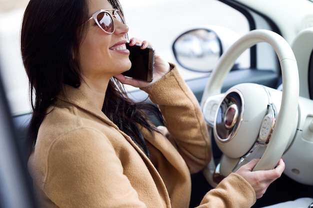 Schöne junge Frau, die ihren Handy im Auto verwendet.