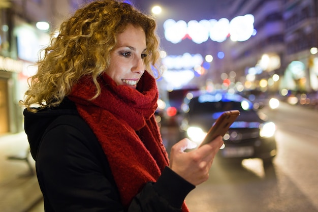 Schöne junge Frau, die ihren Handy in der Straße nachts verwendet.