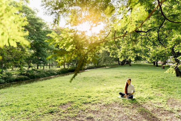 Schöne junge Frau, die im Frühling oder Sommer bei Sonnenaufgang in einem Park meditiert