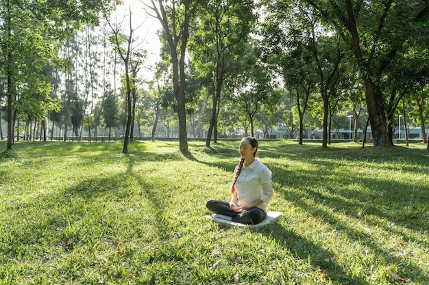 Schöne junge Frau, die im Frühling oder Sommer in einem Park bei Sonnenuntergang meditiert