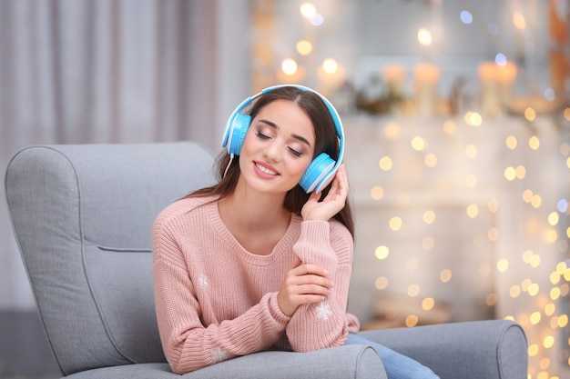 Schöne junge Frau, die im weihnachtlich dekorierten Wohnzimmer Musik hört