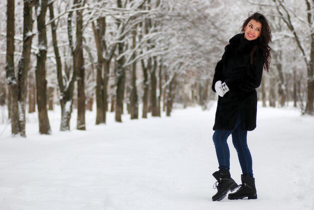 Schöne junge Frau, die in den schneebedeckten Park des Winters geht