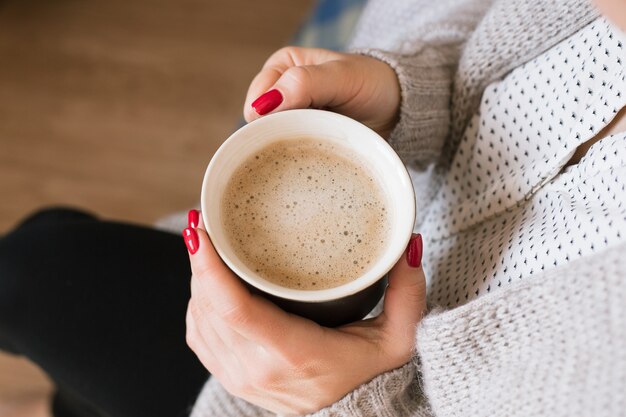 Schöne junge Frau, die Kaffee-Cappuccino trinkt, perfekte rote Gellackmaniküre.